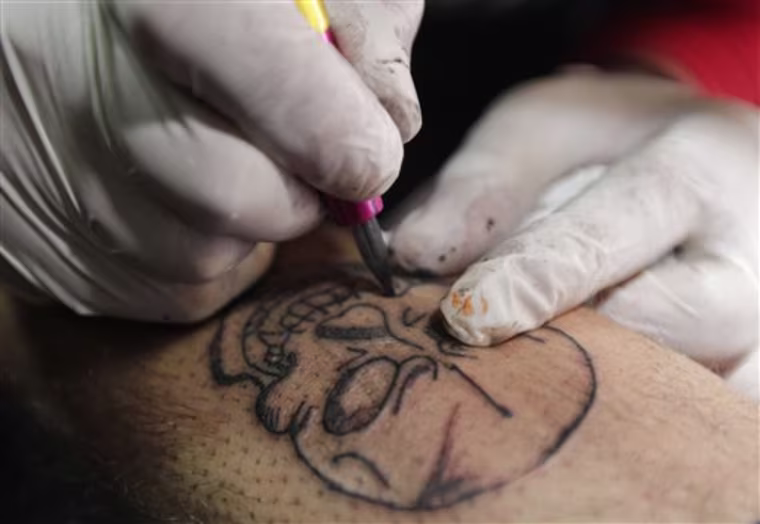 In this Monday, Nov. 14, 2011 photo, Mohammed Abass, 28, draws a tattoo of a skull on Saad Saif's leg, 25, in Baghdad, Iraq.  After more than eight years in Iraq, the departing American military's legacy includes a fledgling democracy, bitter memories of war, and for the nation's youth, rap music, tattoos and slang. (AP Photo/Hadi Mizban)